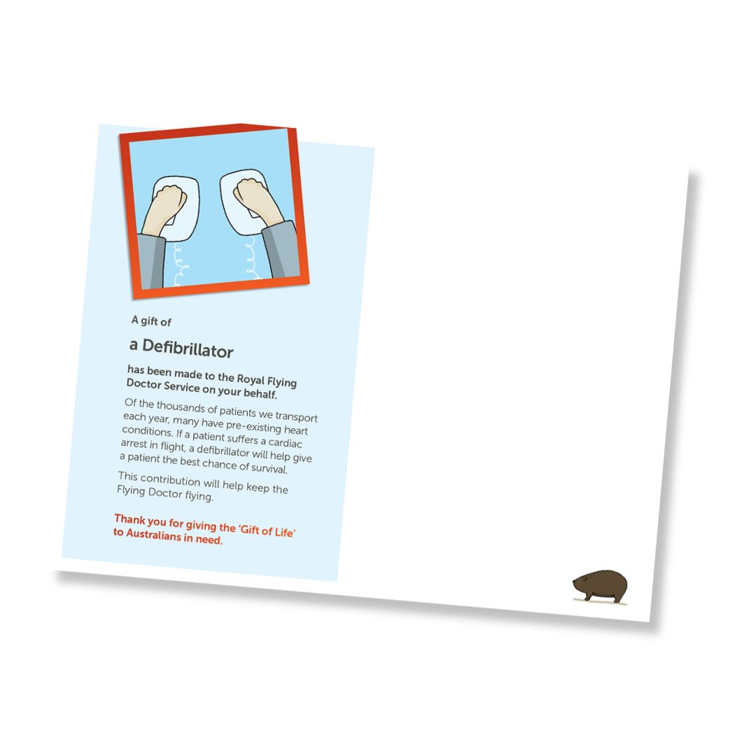 Inside of a card for a defibrillator donation to the Royal Flying Doctor Service, shown at an angle on a white background. The card features a light blue background with text, an illustration of a defibrillator, and a small brown wombat in the bottom right corner.