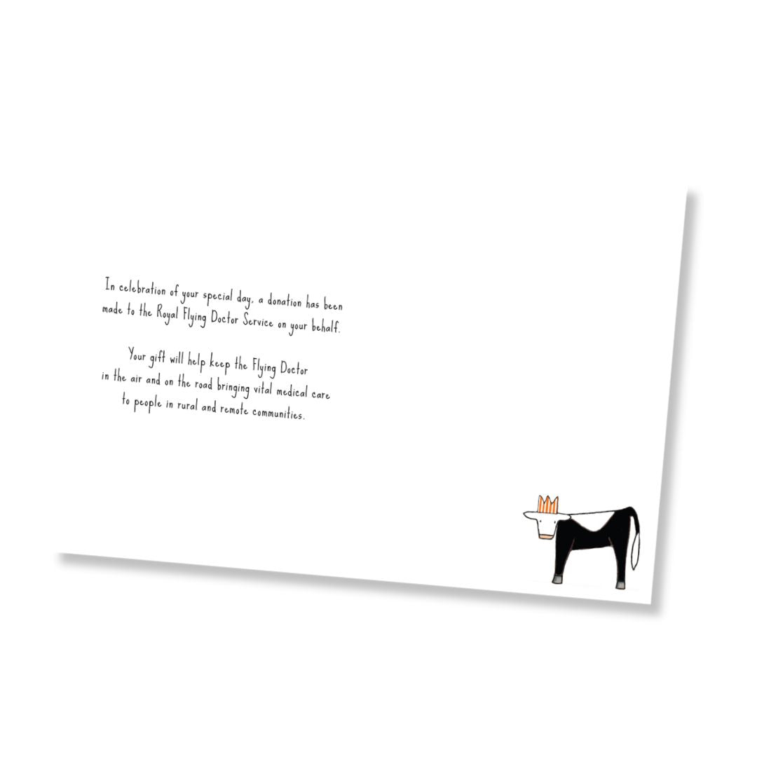 Inside of a white greeting card shown at an angle on a white background, featuring black printed text that says, "In celebration of your special day, a donation has been made to the Royal Flying Doctor Service on your behalf. Your gift will help keep the Flying Doctor in the air and one the road bringing vital medical care to people in rural and remote communities." on the left and a small illustration of a black and white cow with a red stripy crown on the bottom right.