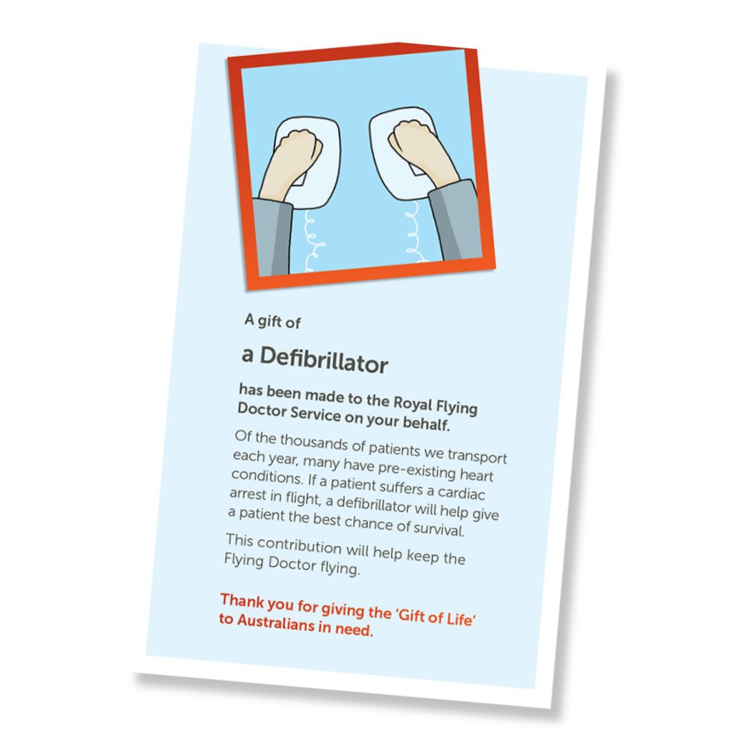 A card for a donation of an defibrillator, shown at an angle on a white background. The card has a pale blue field, a small illustrated header with hands on defibrillator paddles, and a red-orange border, and text stating it is a gift of a defribillator and a that it is a donation to the Royal Flying Doctor Service.
