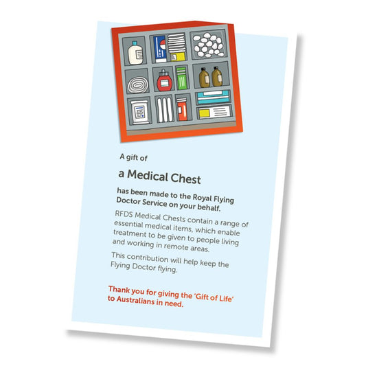 A card for a donation of a medical chest, shown at an angle on a white background. The card has a pale blue field, a small illustrated header with medical equipment in a tub, and a red-orange border, and text stating it is a gift of amedical chest and a that it is a donation to the Royal Flying Doctor Service.