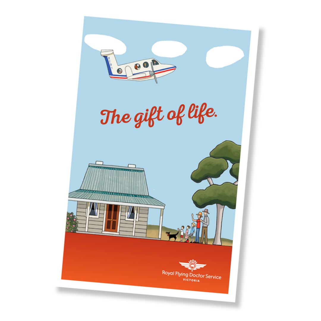A greeting card with an illustrated scene showing an RFDS plane, house, trees, and people, with the text 'The gift of life.' and 'Royal Flying Doctor Service Victoria' at the bottom, shown against a plain white background.