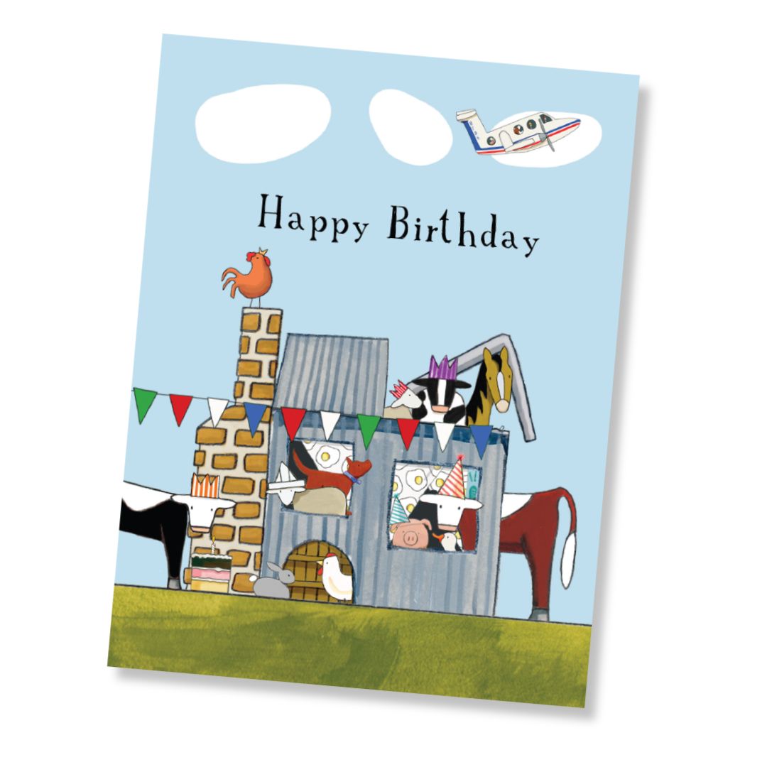 A Happy Birthday greeting card featuring a whimsical farm scene with cows, a chicken, a pig, a rooster, an RDFS plane, and bunting under a light blue sky. The card is shown at a slight angle on a white background.