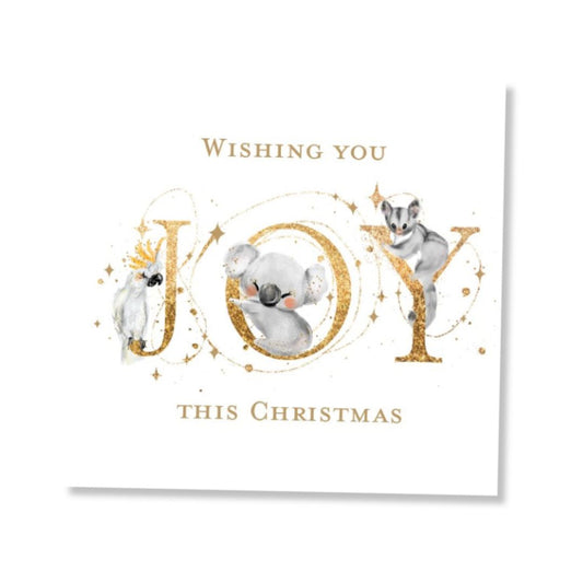 A square white Christmas greeting card featuring the word 'JOY' in large gold glitter letters, decorated with a cockatoo, koala and ring-tail possum nestled within the letters. The text reads 'Wishing you JOY THIS CHRISTMAS' in gold.